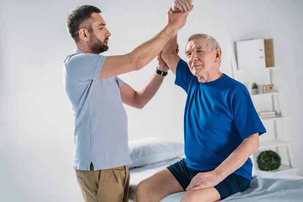 Retrato del terapeuta de rehabilitación haciendo masaje al hombre mayor en la mesa de masaje - foto de stock