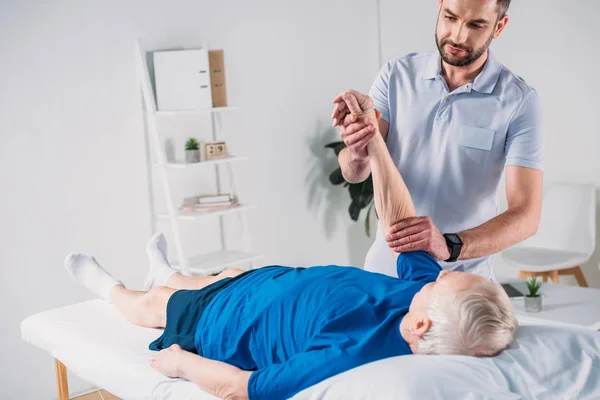 Focused physiotherapist doing massage to senior man on massage table — Stock Photo