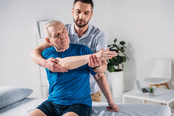 Retrato del fisioterapeuta haciendo masaje al hombre mayor en la mesa de masaje - foto de stock