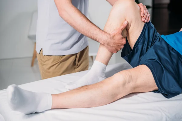 Tiro cortado de fisioterapeuta fazendo massagem ao homem sênior na mesa de massagem — Fotografia de Stock