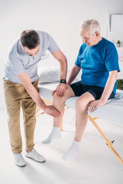 Terapeuta de rehabilitación haciendo masaje al hombre mayor en la mesa de masaje - foto de stock