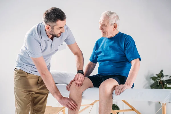 Портрет реабилитационного терапевта, делающего массаж пожилому человеку на массажном столе — стоковое фото