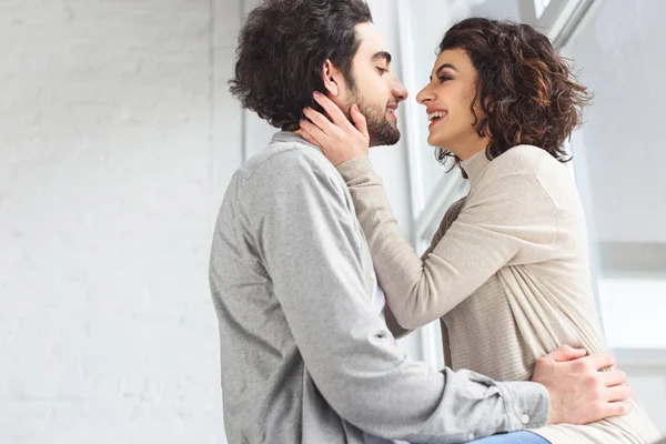 Feliz pareja joven abrazándose y mirándose en casa - foto de stock