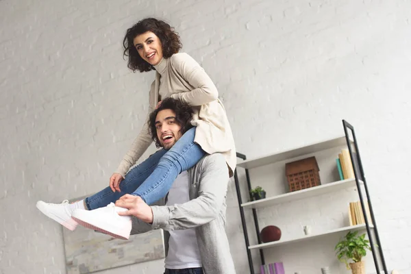 Sonriente novia sentado en novios hombros en casa - foto de stock