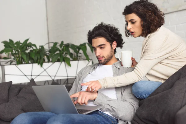 Junges Paar zeigt daheim auf etwas am Laptop — Stockfoto