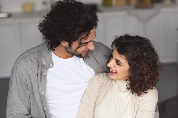 Lächelndes junges Paar, das sich zu Hause umarmt und einander ansieht — Stockfoto