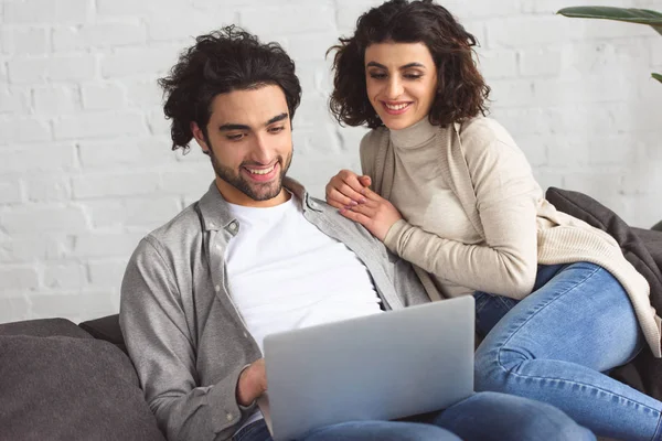 Улыбающаяся молодая пара смотрит на ноутбук дома — стоковое фото