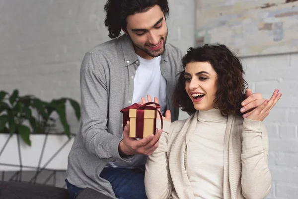 Boyfriend presenting gift to surprised girlfriend at home — Stock Photo