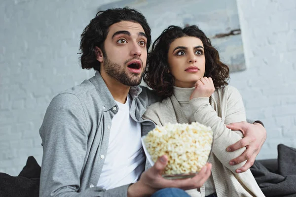 Jeune couple tenant bol avec pop-corn et regarder un film d'horreur à la maison — Photo de stock