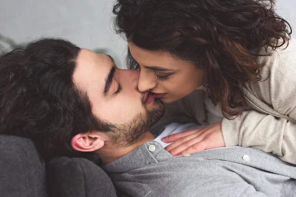 Joven pareja mintiendo y besándose en casa - foto de stock