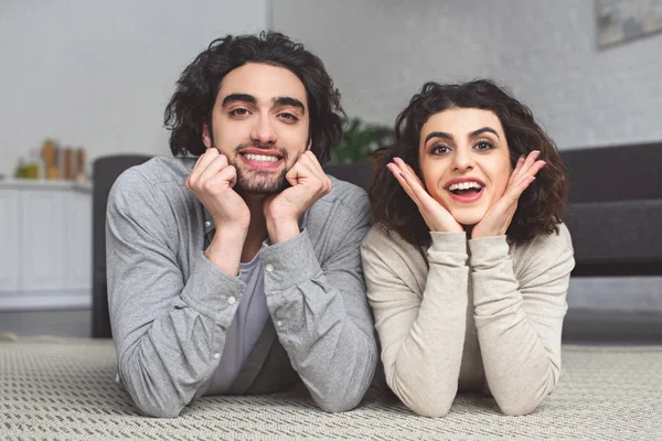 Happy young couple lying on floor and looking at camera at home — Stock Photo