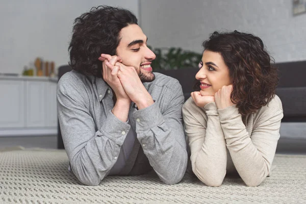 Lächelndes junges Paar, das auf dem Boden liegt und sich zu Hause anschaut — Stockfoto