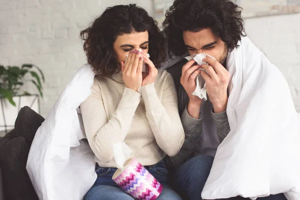 Enferma joven pareja soplando narices en servilletas en casa - foto de stock