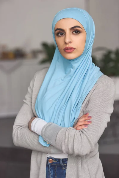 Красивая серьезная мусульманка в хиджабе стоит со скрещенными руками и смотрит в сторону дома — стоковое фото