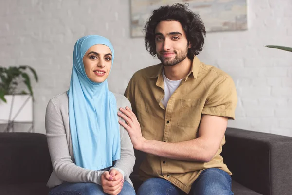 Muslim couple sitting on sofa and looking at camera at home — Stock Photo