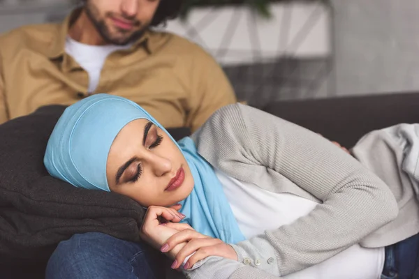 Muslim girlfriend in hijab sleeping on boyfriends legs at home — Stock Photo