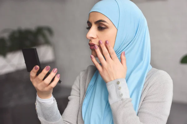 Schöne muslimische Frau im Hidschab schaut zu Hause in den Spiegel — Stockfoto