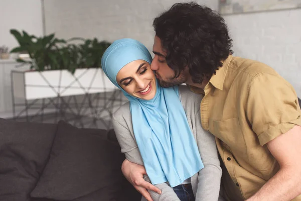 Muslim boyfriend kissing girlfriend in hijab at home — Stock Photo