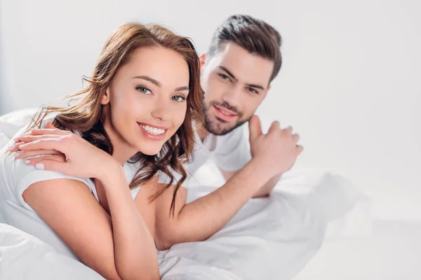 Portrait of smiling young couple looking at camera while resting on bed isolated on grey — Stock Photo