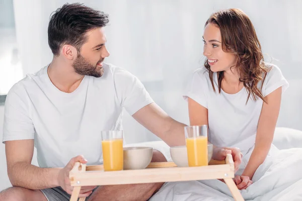 Young man brought breakfast in bed for smiling girlfriend — Stock Photo