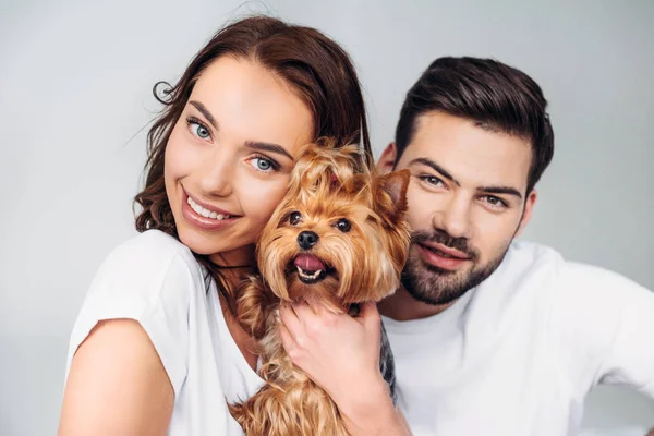 Ritratto di giovane coppia sorridente con yorkshire terrier guardando la fotocamera isolata su grigio — Foto stock