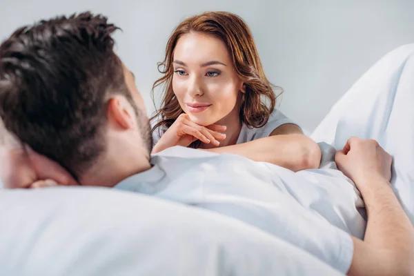 Jovem bonita mulher apoiando-se no namorado, enquanto descansando na cama juntos isolado no cinza — Fotografia de Stock