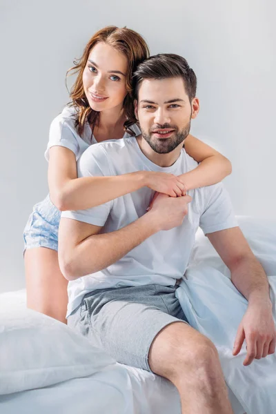 Portrait de jeune jolie femme étreignant petit ami sur lit isolé sur gris — Photo de stock