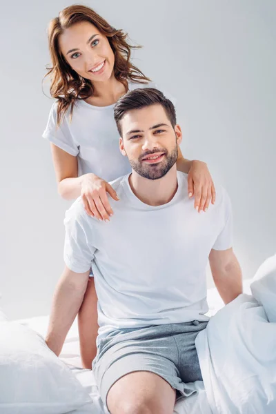 Junge hübsche Frau umarmt Freund auf Bett isoliert auf grau — Stockfoto