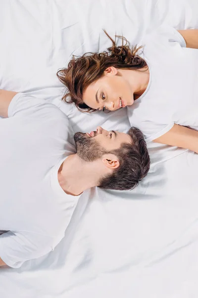 Vista aérea de la joven pareja enamorada mirándose mientras yacen juntos en la cama - foto de stock