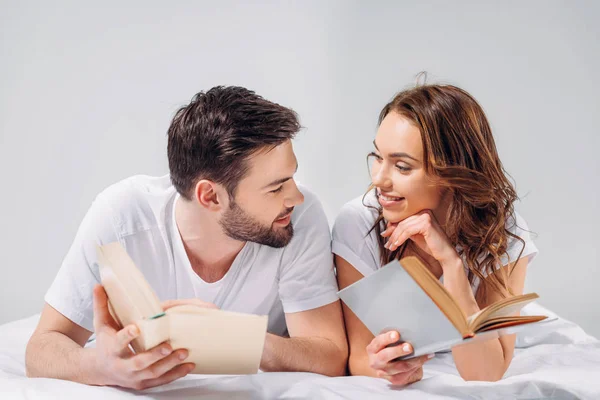 Portrait of young smiling couple with books lying on bed isolated on grey — Stock Photo