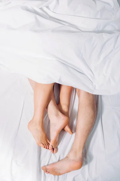 Cropped shot of female and male legs in bed — Stock Photo