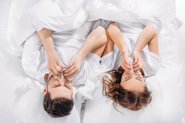 Visão aérea do casal com tecidos deitados na cama enquanto está resfriado — Fotografia de Stock