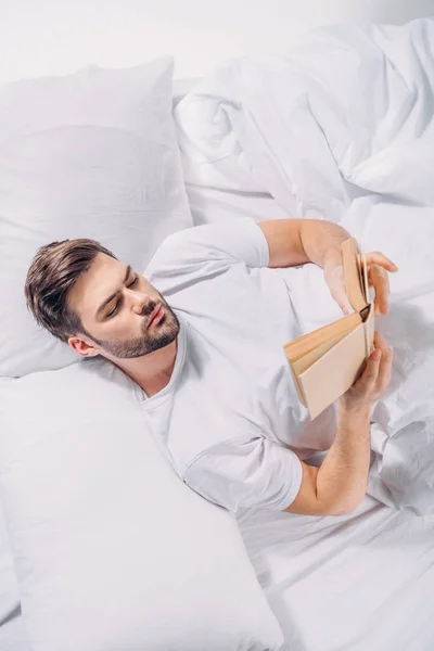 Blick über den Kopf eines fokussierten jungen Mannes, der Buch im Bett liest — Stockfoto