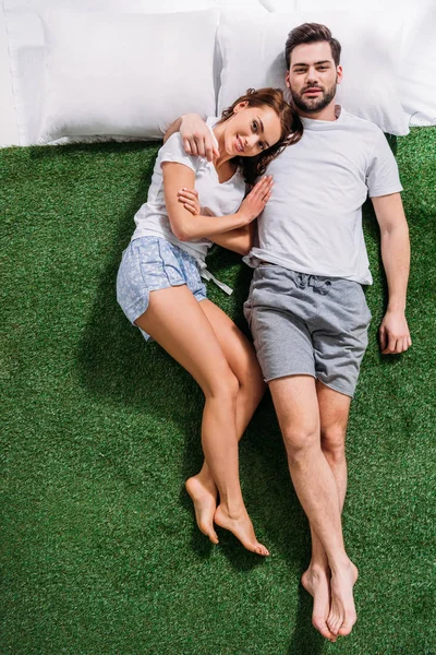 Overhead view of young couple in love lying on pillows on green grass — Stock Photo