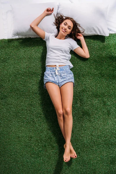 Overhead view of young smiling woman resting on pillows on green lawn — Stock Photo