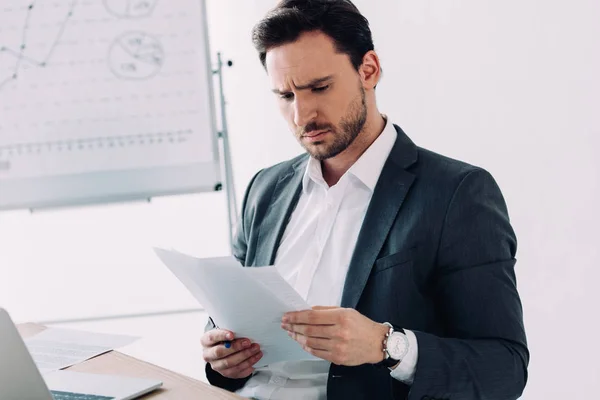 Серьезный привлекательный бизнесмен читает документы в офисе — стоковое фото