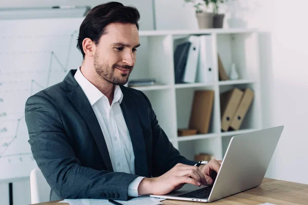 Vista lateral del hombre de negocios guapo que trabaja con el ordenador portátil en la oficina - foto de stock