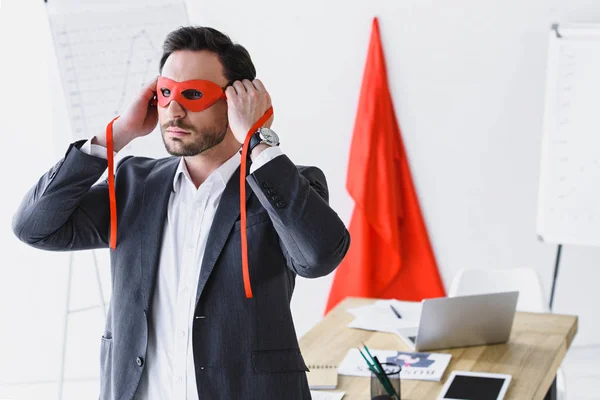 Супер бизнесмен связывая красную маску в офисе — стоковое фото