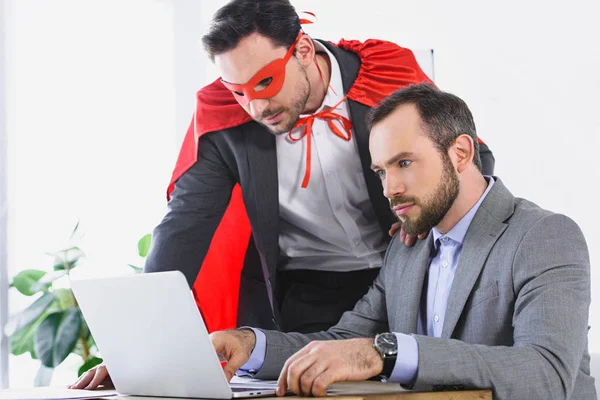 Супер бізнесмен в масці і накидку допомагає бізнесмену з роботою в офісі — стокове фото