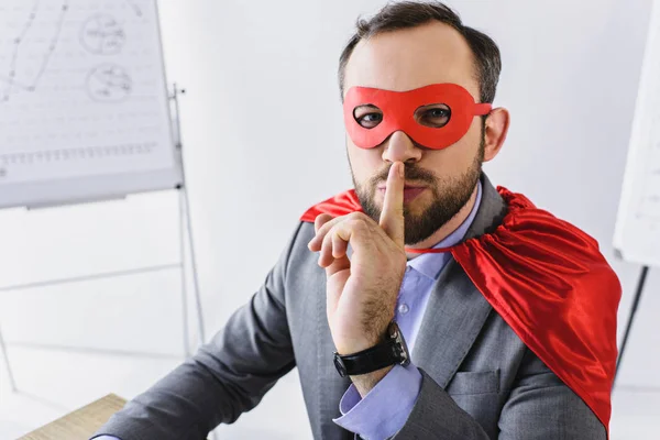 Super homme d'affaires en masque et cape montrant signe de silence dans le bureau — Photo de stock