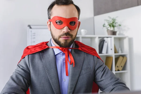 Porträt eines Superunternehmers in Maske und Umhang, der im Büro in die Kamera blickt — Stockfoto