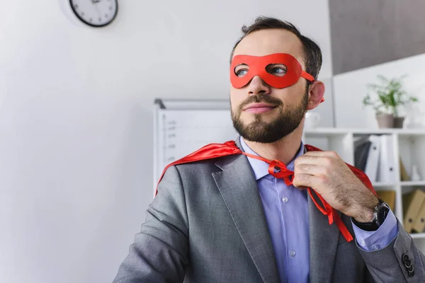 Glücklicher Superunternehmer in Maske und Umhang, der im Büro wegschaut — Stockfoto