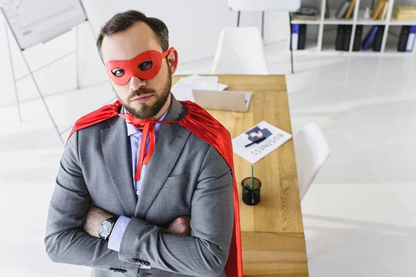 Hochwinkelaufnahme des Superunternehmers in Maske und Umhang, der im Büro in die Kamera schaut — Stockfoto