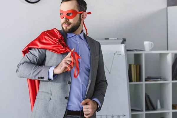 Superunternehmer mit Maske, Umhang auf der Schulter und im Büro wegguckend — Stockfoto