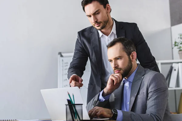 Handsome businessman pointing on something at laptop to colleague in office — Stock Photo