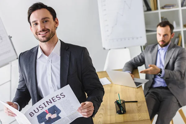 Gutaussehende Geschäftsleute mit Zeitung und Laptop im Büro — Stockfoto