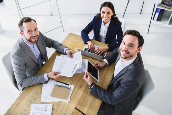 Vista de ángulo alto de los empresarios sonrientes que trabajan con aparatos en la oficina - foto de stock