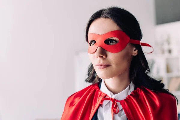 Porträt einer attraktiven Superunternehmerin in Umhang und Maske, die im Büro wegschaut — Stockfoto