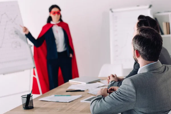 Super empresária em máscara e capa mostrando apresentação para homem de negócios no escritório — Fotografia de Stock