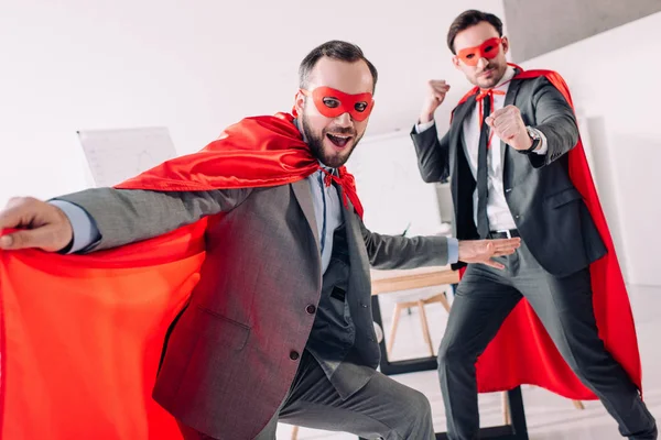 Beaux super hommes d'affaires en masques et capes s'amuser au bureau — Photo de stock